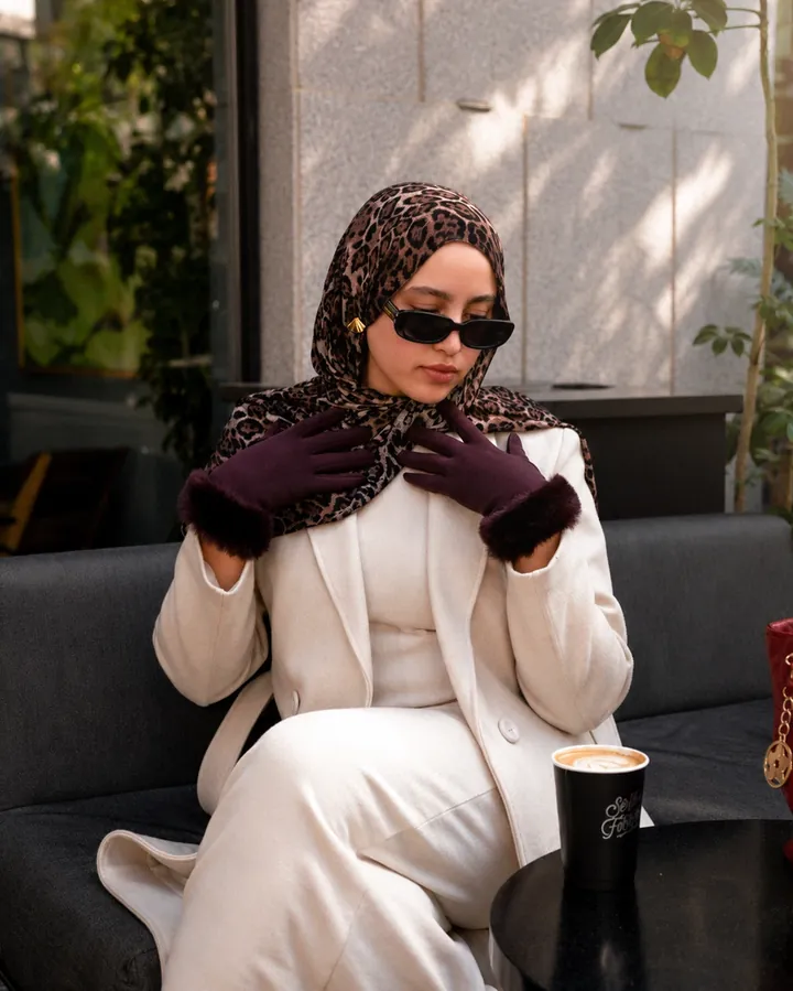 A cream suit with a leopard-print headscarf and burgundy fur-cuffed gloves in a calm café setting.