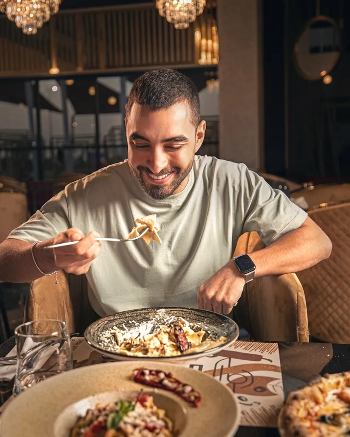 A man eating pasta at a restaurant table with a second plate in front of him.